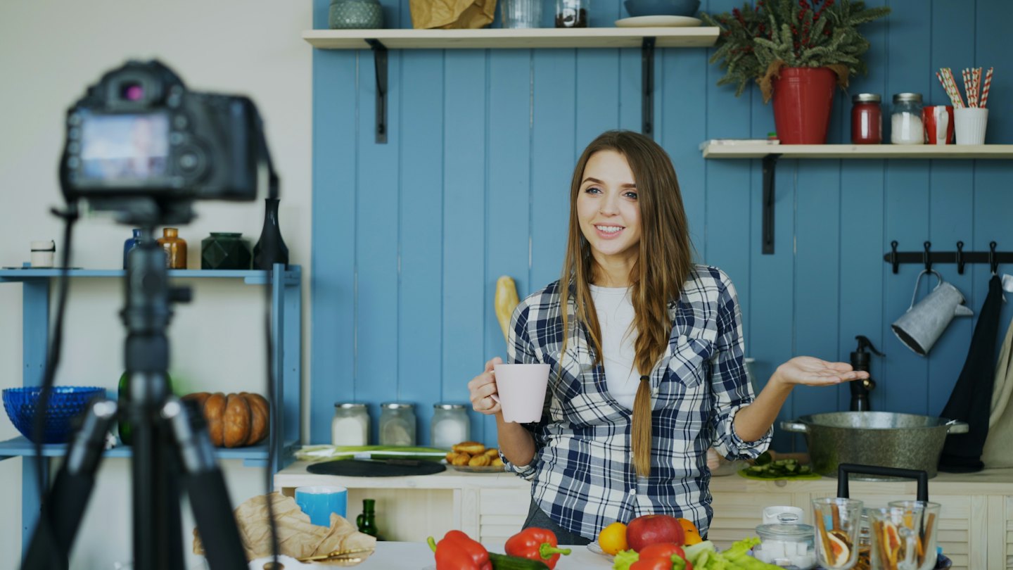 Mujer grabando un vlog en una cocina moderna con productos frescos.