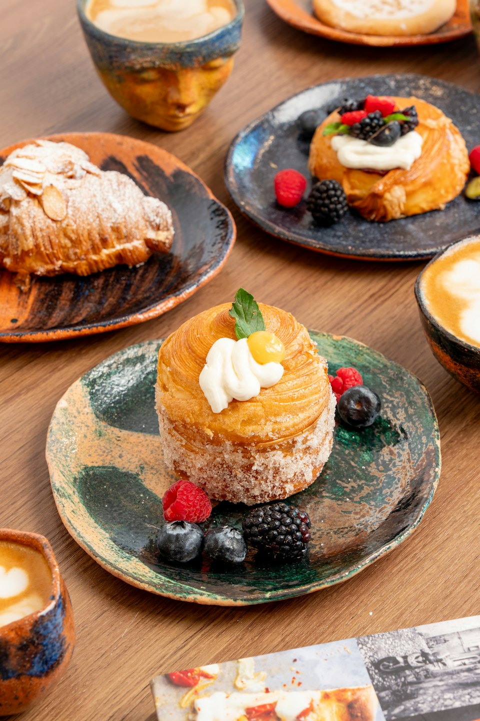 Pasteles y café dispuestos sobre una mesa de madera de cafetería.